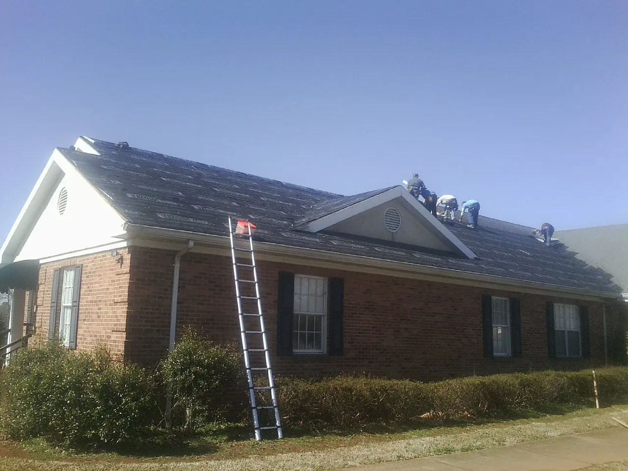 Crew tearing shingles off a brick ranch roof with a ladder set — Metal Roof Repair work by our crew in Ludlow Falls
