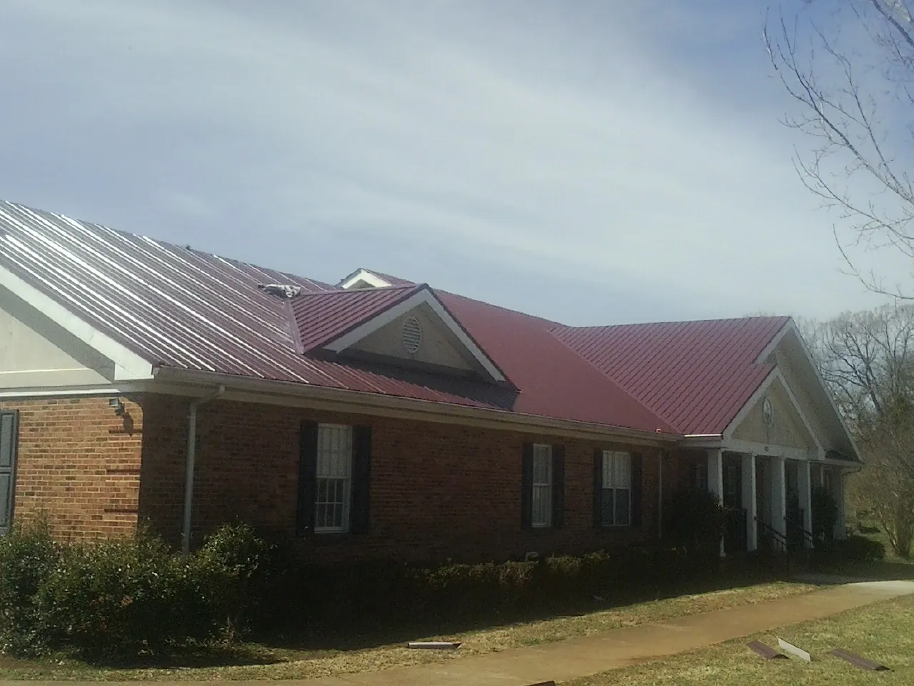 Red metal roof with gabled entries on a long brick building, from a Hail Damage Roof Repair job in Ludlow Falls