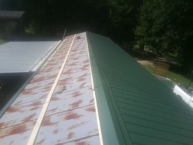 Old rusted panels beside newly installed green metal roofing — Wind Damage Roof Repair by Roofing Brothers in Ludlow Falls
