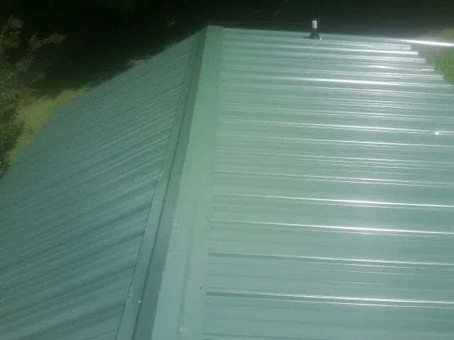 New green metal panels meeting at the ridge of a roof — Flat Roof Repair work by our crew in Ludlow Falls