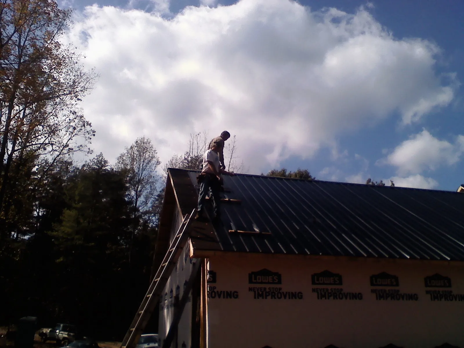 Roofer fastening dark metal panels high against a cloudy sky, from a Roof Inspection job in Ludlow Falls