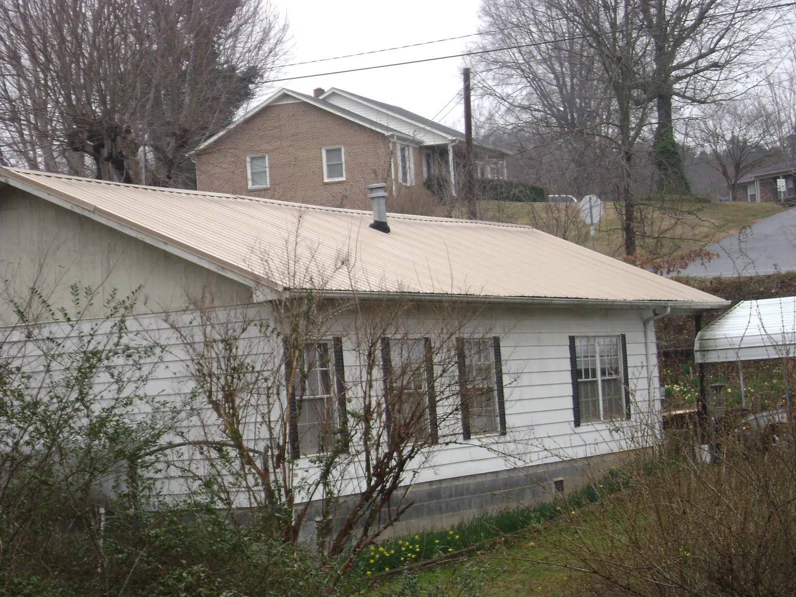 Tan metal roof on a white sided house set into a hillside — Commercial Roofing by Roofing Brothers in Ludlow Falls