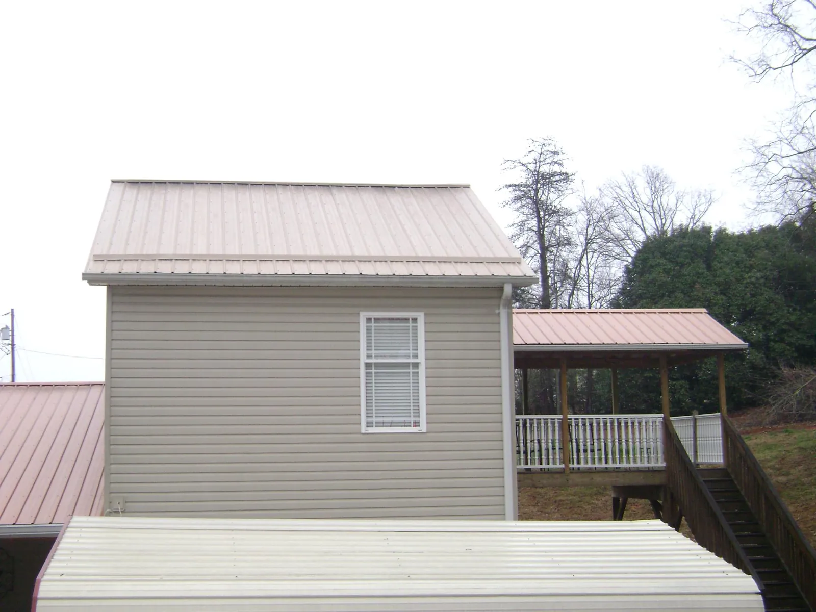 Tan metal roofs on a two story addition and attached porch, from a Roof Replacement job in Ludlow Falls